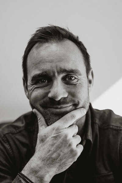 Black and white portrait of a man smiling with his hand on his chin, photographed by Breckenridge branding photo team.