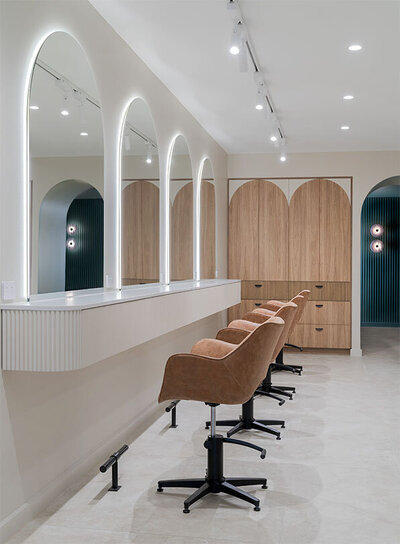 Stylish salon workspace featuring arched illuminated mirrors, tan swivel chairs, and wooden cabinetry, ideal for women's hair consultations and styling in Sydney.
