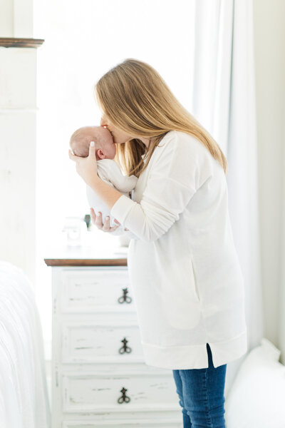 Mother tenderly kisses newborn during well lit in home newborn session.