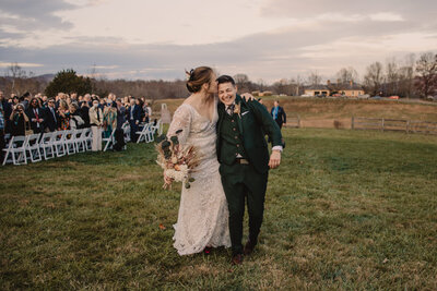 A newlywed couple walking with their arms around each other as one kisses the other's head 