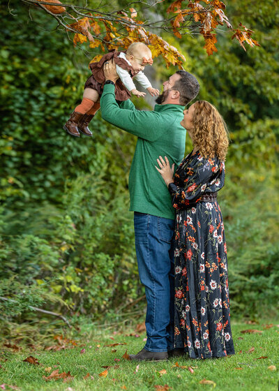 A husband and wife are standing in the forest playing with their baby daughter in the air