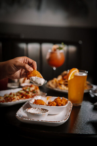 Juicy bacon cheeseburger topped with a cherry tomato and pickle skewer, served alongside crispy golden fries in a tin and a refreshing cold beer.