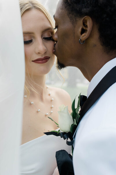 A groom kissing his bride on the cheek on their wedding day.