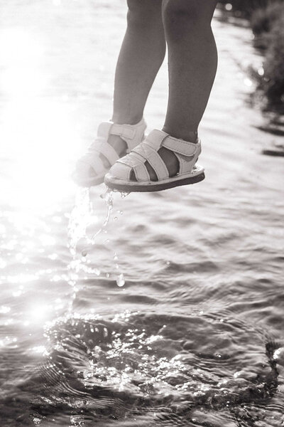 A little girls feet in white sandals splashing in the water