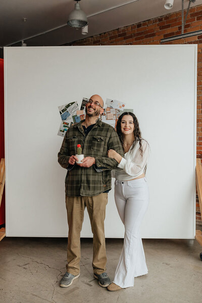 Taysha and Husband smiling at the camera holding one another. Husband is holding a small cactus with a red flower on top of it.