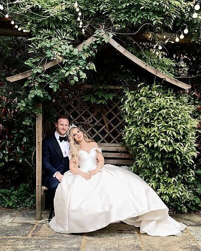 bride and groom sitting on bench surrounded by leafy shrubs