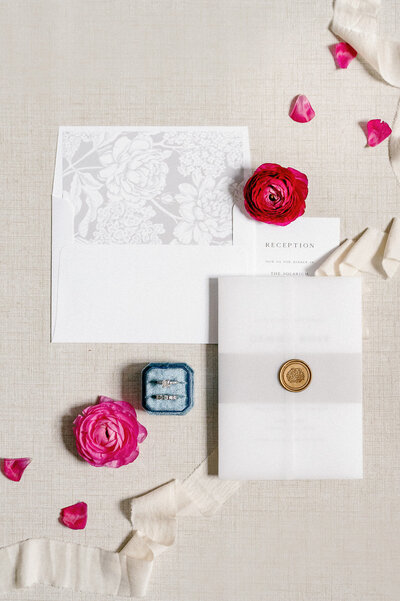 a flat lay of pink flowers, wedding stationery, and wedding rings