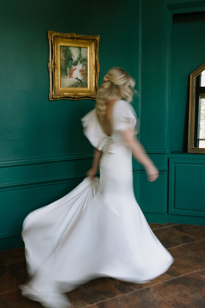 Bride spins holding wedding dress in green gallery with gold frames.