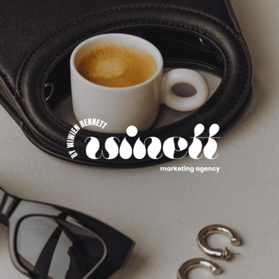 A white cup of espresso sits on a black handbag with the Winn Bennett Marketing Agency logo, surrounded by sunglasses and earrings. The image evokes a sophisticated and stylish brand identity.