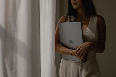 woman holding a laptop looking out window