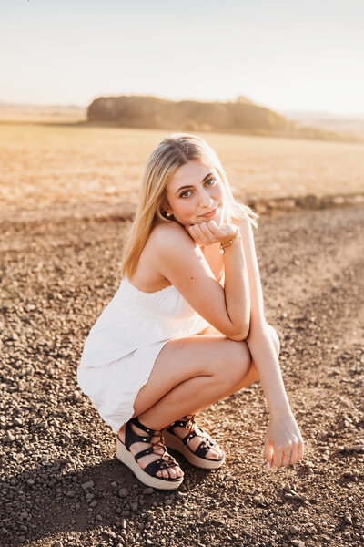 Senior Photography Services in Salem, girl in white dress kneeling down on dirt road