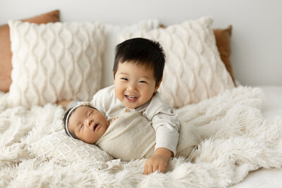 big baby brother smiling with newborn brother on bed