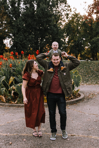 Family photo of a mom and dad walking with a baby on the dad's shoulders in Allegheny Commons Park. 