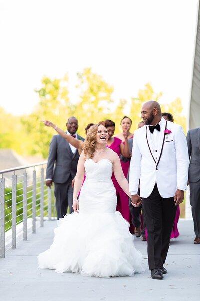 African American couple dressed in white celebrate their wedding with their bridal party dressed in gray and magenta