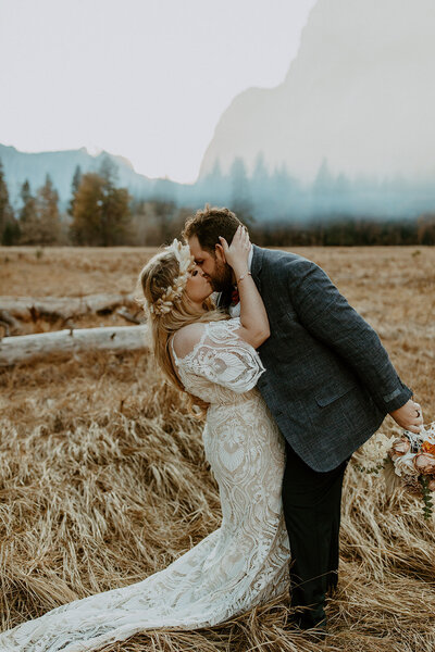 bridal couple embracing in front of pine trees