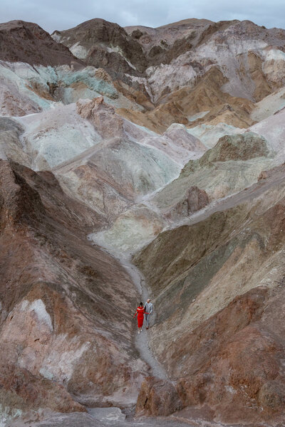 A couple walks hand-in-hand up a rocky path surrounded by the colorful hills of Artists Palette in Death Valley