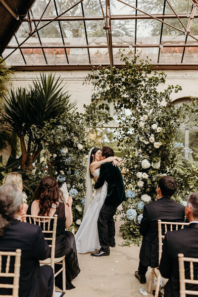 A bride smiles a big grin at the camera, holding her bouquet with her bridesmaids