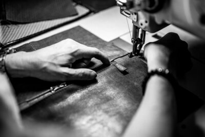 Hands of a leather bag creator sewing with her sewing machine.