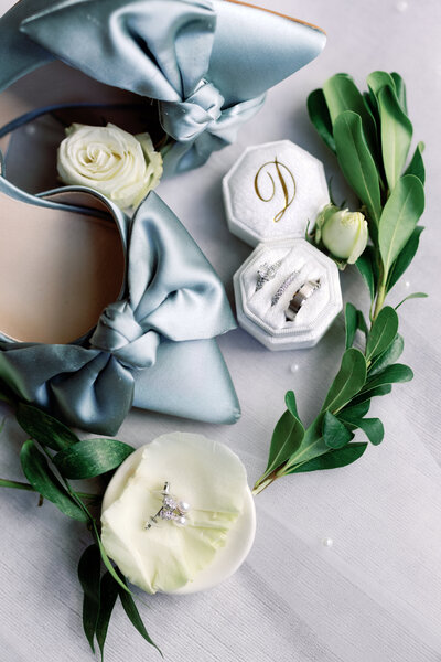 Close-up of wedding day details including a ring box, dusty blue ribbon, and soft white flowers styled flat on a table