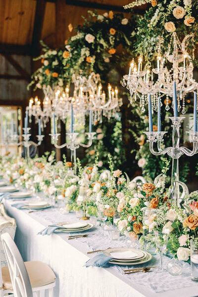 Elaborate table setting with floral orange, white and green centerpieces and floral arrangements hanging from the chandeliers