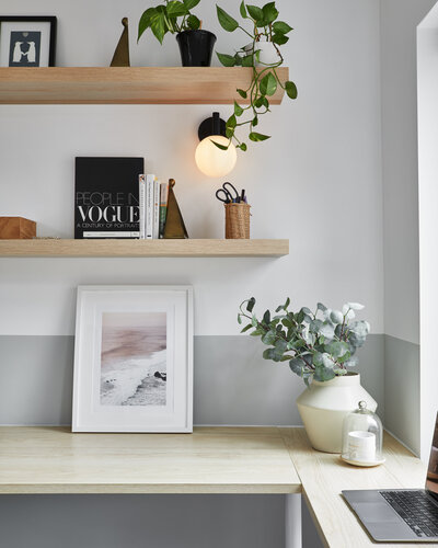 Decorative art and a potted plant sitting atop a light stained wood desk. A globe pendant light fixture and two floating shelves containing various books, art pieces, and potted plants hang above the desk.