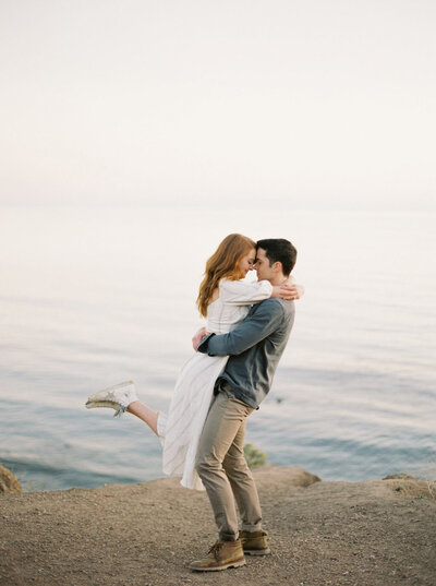 engaged couple hugging on beach with  high top shoes
