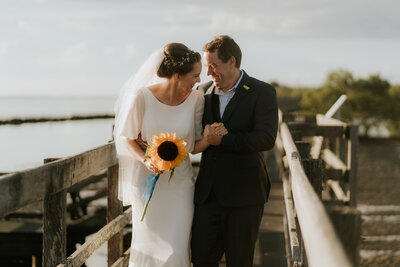 A candid and joyful photo of two newlyweds on Urunga boardwalk during their wedding photography session. They are looking at each other and laughing.