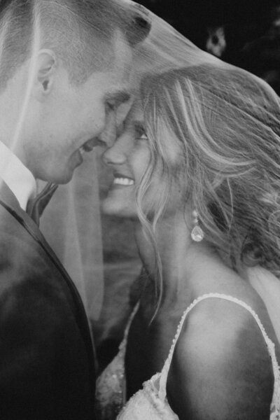 Black and white photo of groom and bride underneath veil smiling at each other by Iowa City wedding photographer Sabrina Wilham