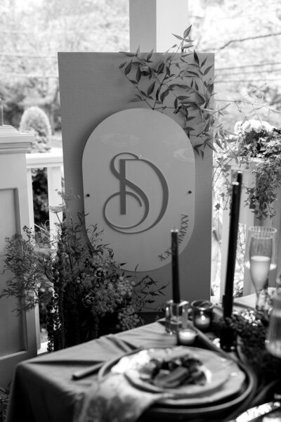 Black and white photo of a custom wedding welcome sign with florals, couple’s initials, and date at the Inn at Hastings Park — designed by Cove Mill Design Co. for a Lexington, MA celebration.