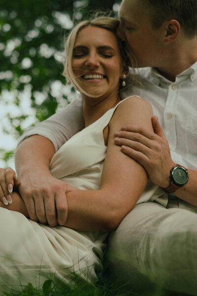 fiance holds bride in a close side hug and kisses her forehead as she smiles
