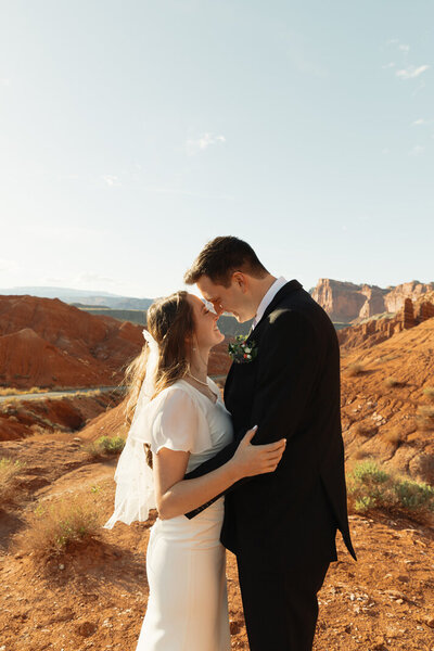 A bride and groom facing each other, with their noses touching as it their almost about to kiss. Behind them, the beautiful and rugged landscape of Captiol Reef National Park located in Torrey, Utah.