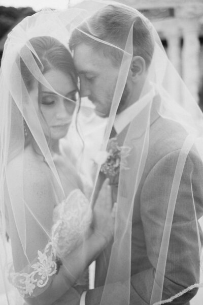 black and white photo of a  bride and groom embracing under the brides veil