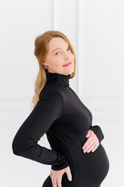 Stunning studio image of a pregnant mom holding her belly and smiling at the camera