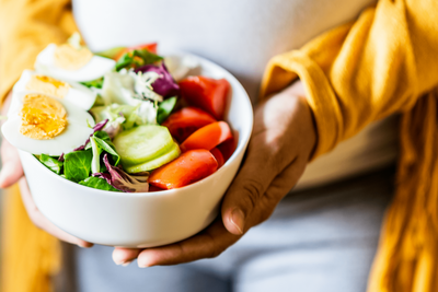 Woman of color holding bowl of healthy food like a salad and toppings.
