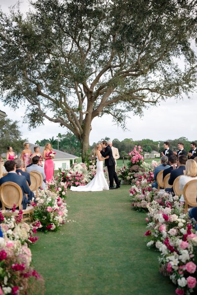 Pink floral lined ceremony with bride and groom sharing first kiss