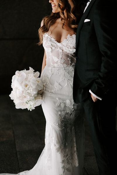 Detail of a bride in an all lace gown, holding a white bouquet of orchids and roses