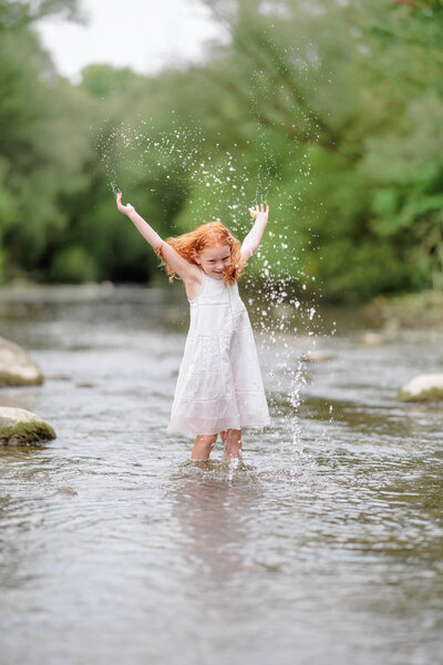 A young girl splashing and playing happily in the water in a river during a photo session with Shannon Cliffe Photography