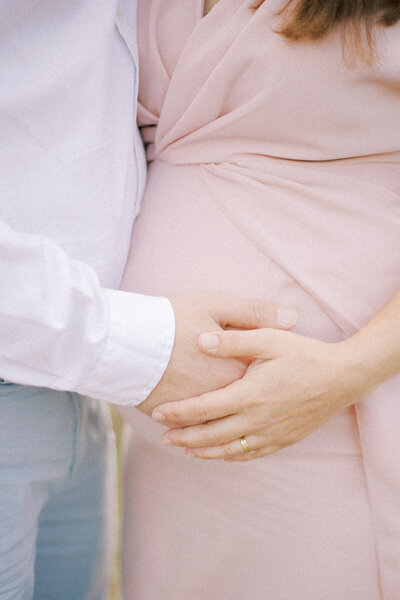 Een close-up van een zwangere vrouw in een elegante witte jurk, met een zachte achtergrond die een rustieke sfeer benadrukt.