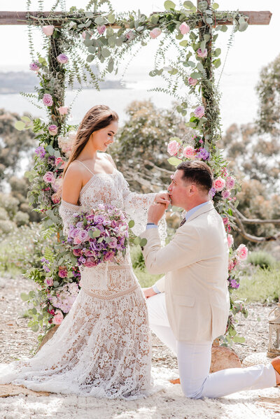 groom kneeling on ground while kissing bride's hand