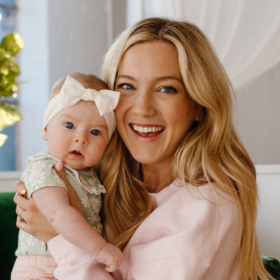 Blonde woman holding her baby with white bow
