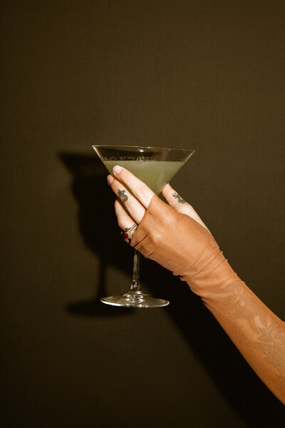 lady holding martini glass agains black wall