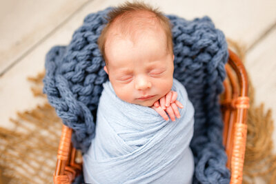 7 day old newborn boy wrapped in a blue swaddle with fingers out in a bamboo basket in Savannah, Ga