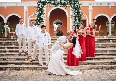 bride and groom kissing with bridal party standing on stairs in background