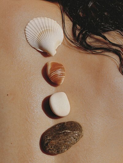 Close-up of shells and stones arranged on sunlit skin, evoking a serene, natural aesthetic with earthy tones and textures.
