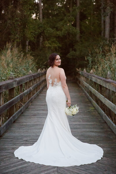 Bride in an illusion gown covered in lace facing away from us but looking back a the camera by Caia Grace