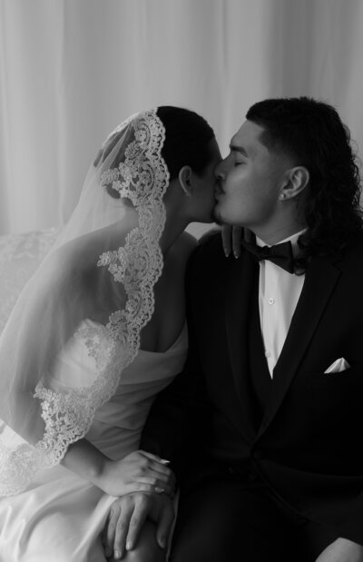 A man kissing a woman wearing a lace veil.