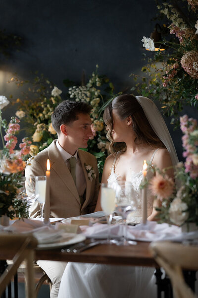 A bride poses and smiles surrounded by lots of greenery and flowers
