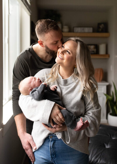 Parents holding newborn by naturally lit window in Portland, Or