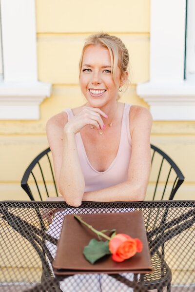 Smiling woman sitting at outside table with notebook and rose