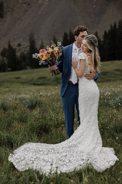 Groom kisses bride on the cheek in front of Rocky Mountain backdrop.